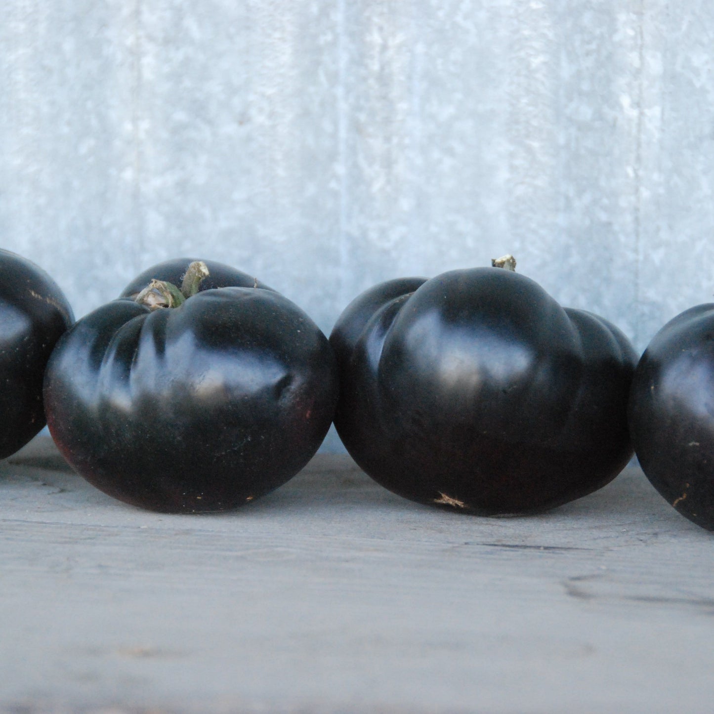 Four black tomatoes lined up on a wooden surface with a light gray background