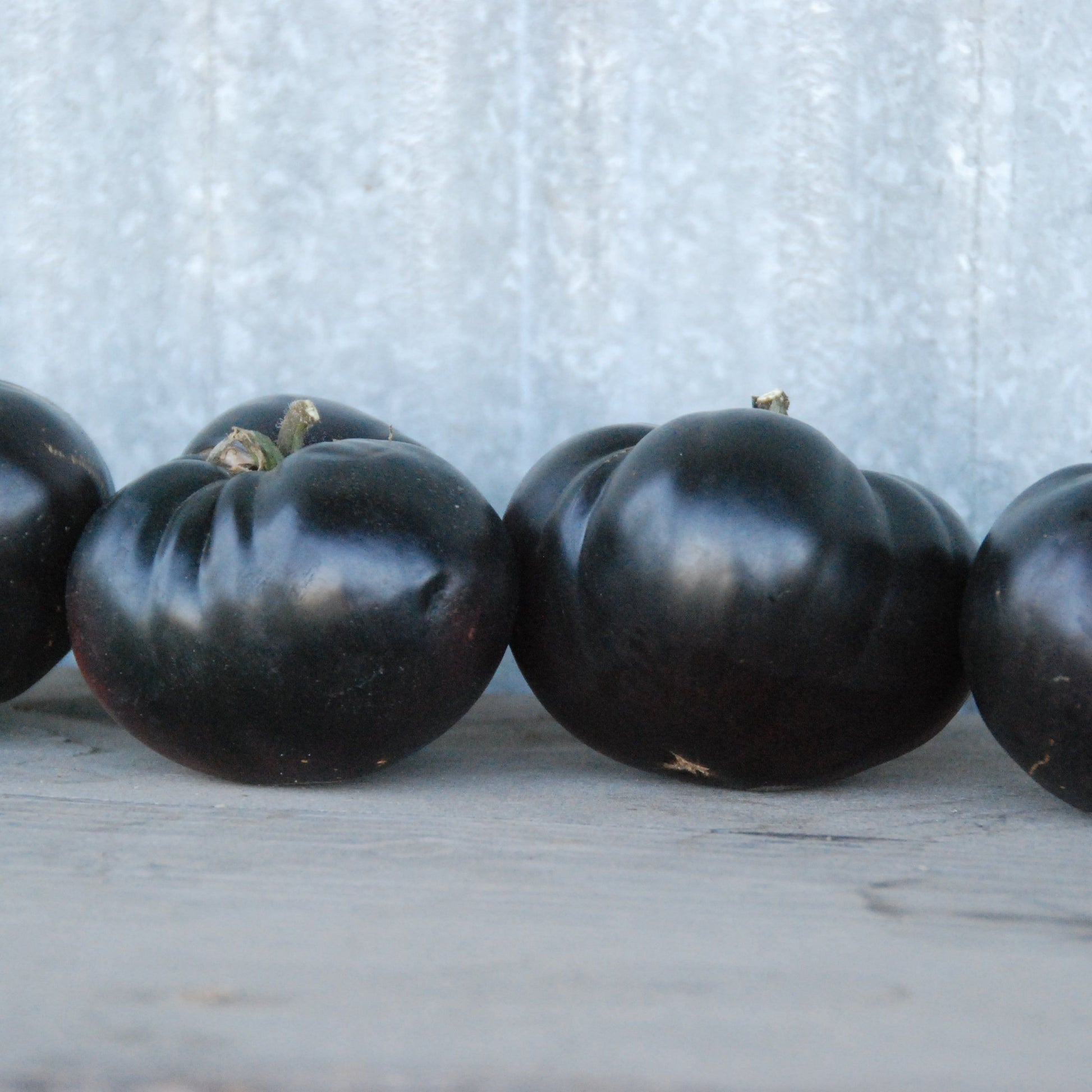 Four black tomatoes lined up on a wooden surface with a light gray background