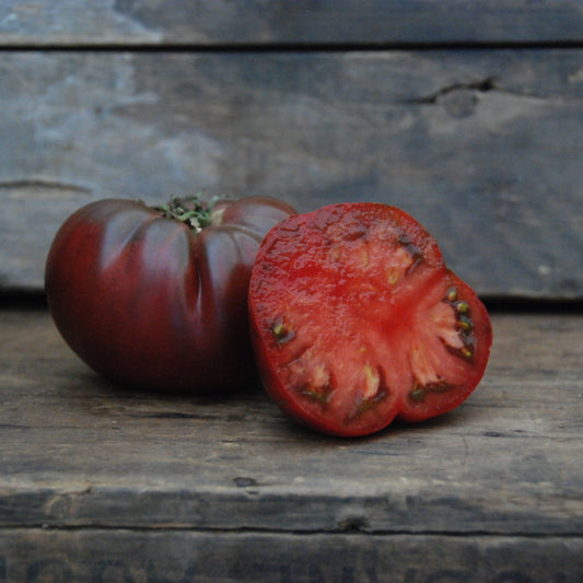 Whole and sliced black tomato on a wooden surface with a rustic background