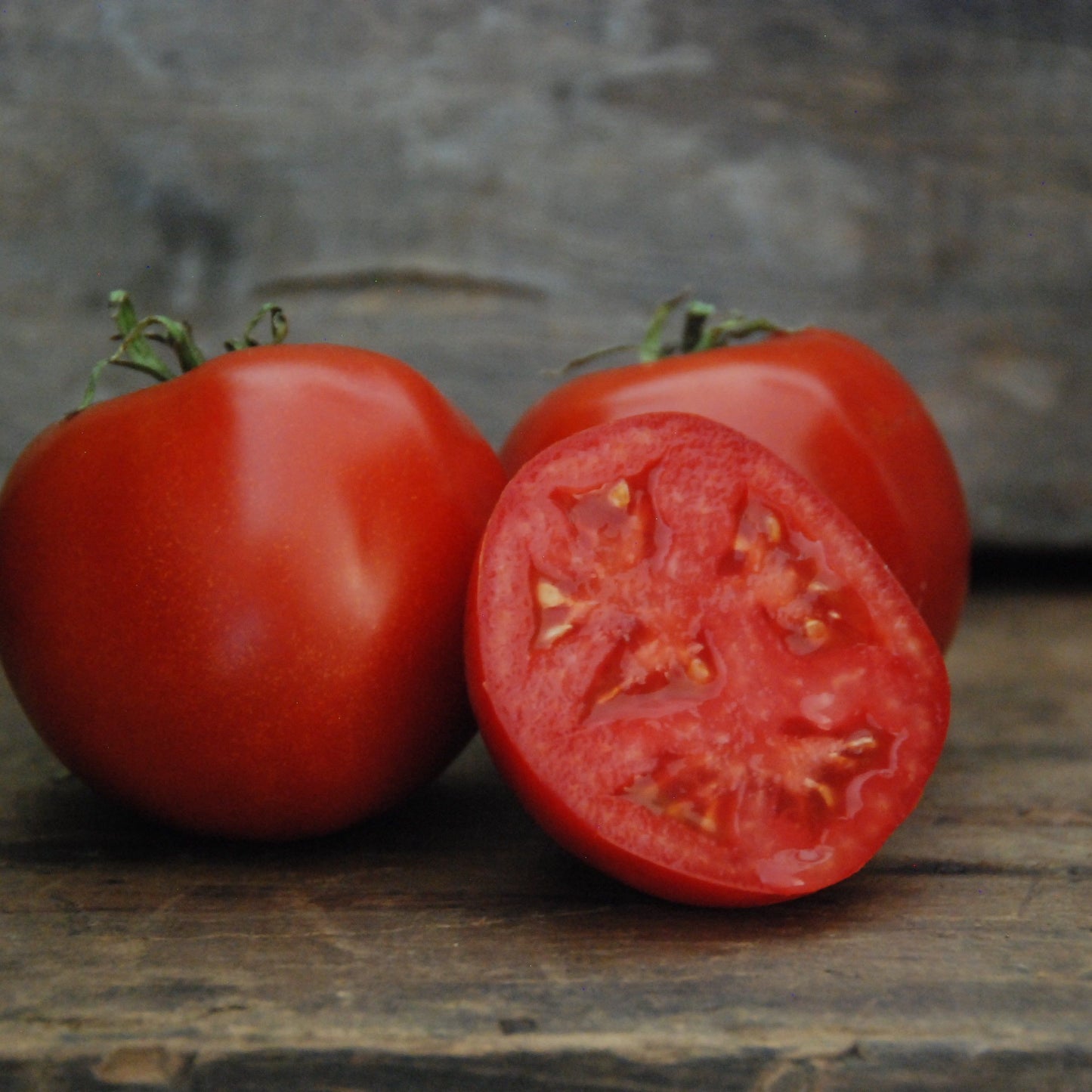 Whole and sliced red tomato on a wooden surface with a stone background
