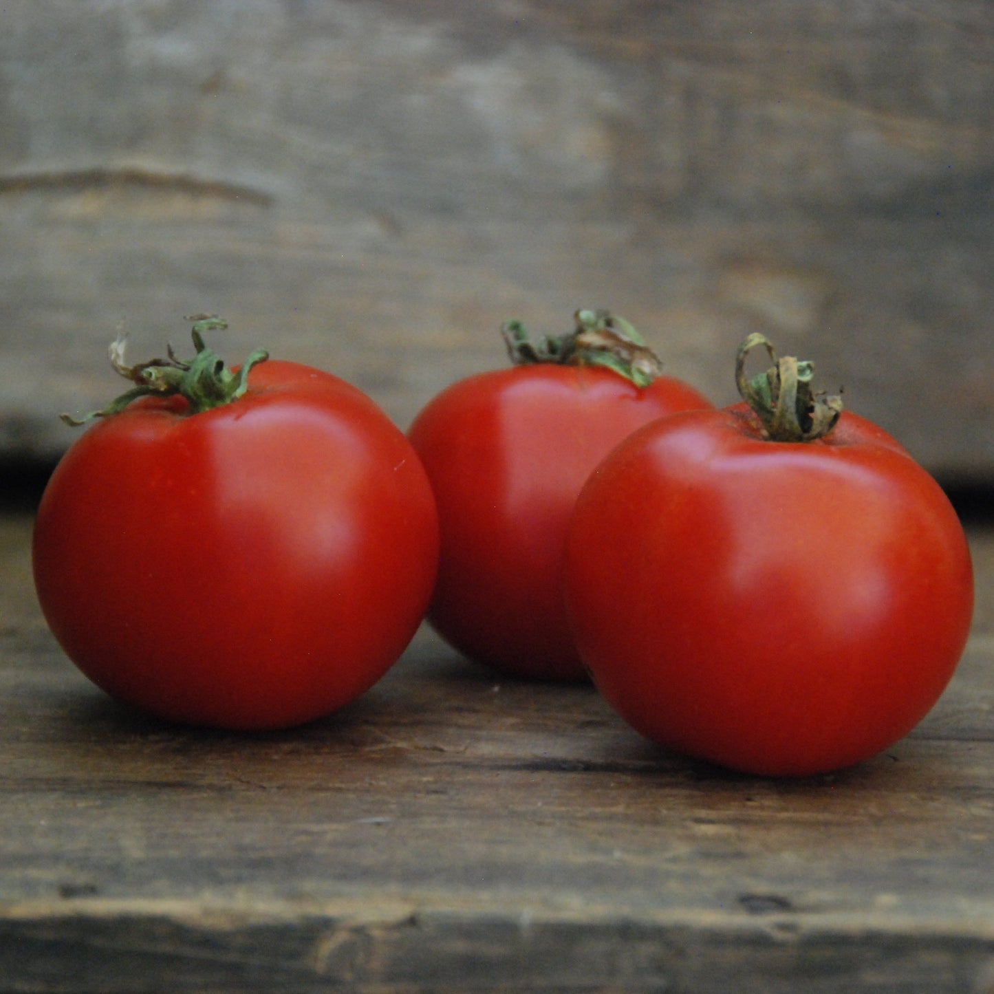 Three red tomatoes on a wooden surface with a blurred stone wall background