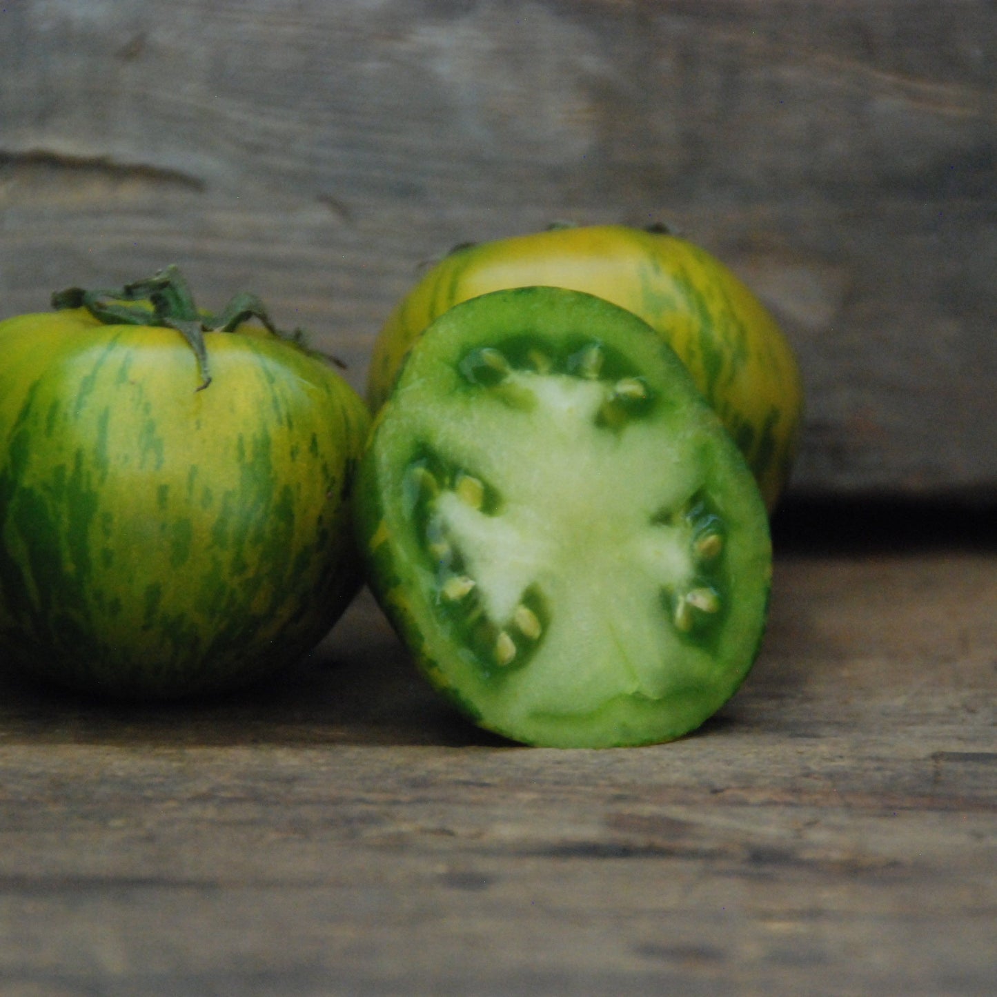 Green tomato with a cut section on a wooden surface