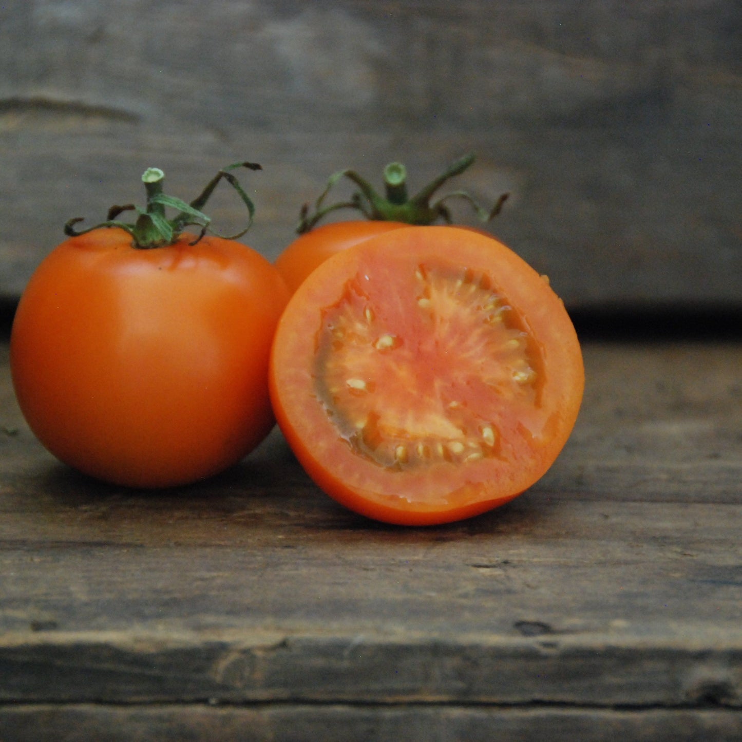 Two tomatoes on a wooden surface, one whole and one cut in half.