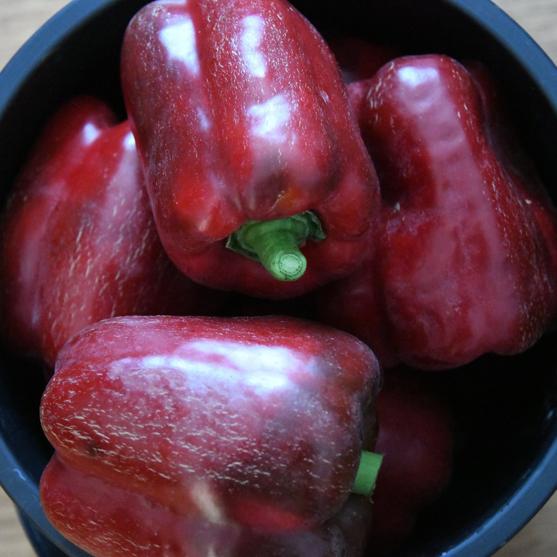 Red bell peppers in a black bowl on a wooden surface