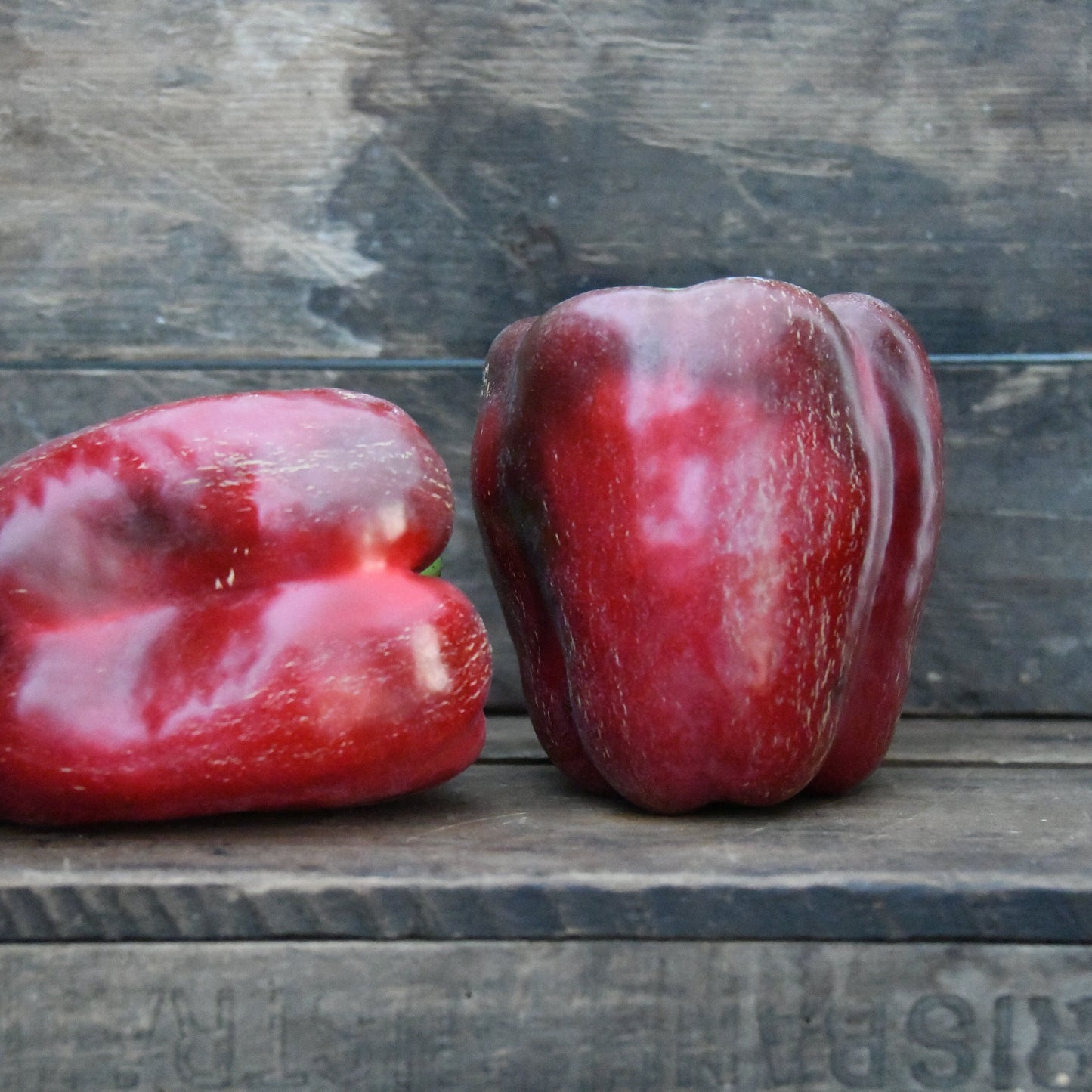 Two red peppers on a wooden surface with a rustic background