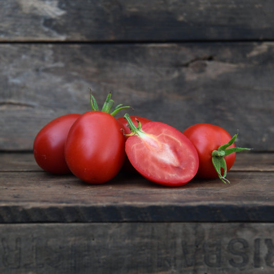five roma tomatoes on a wooden surface with one cut open