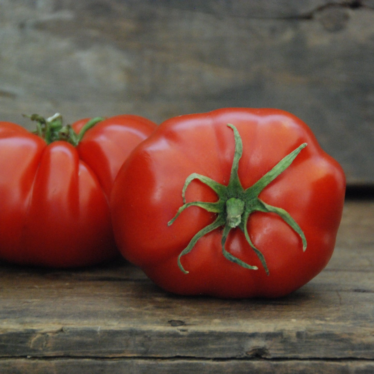 Three red tomatoes on a wooden surface with a stone wall background