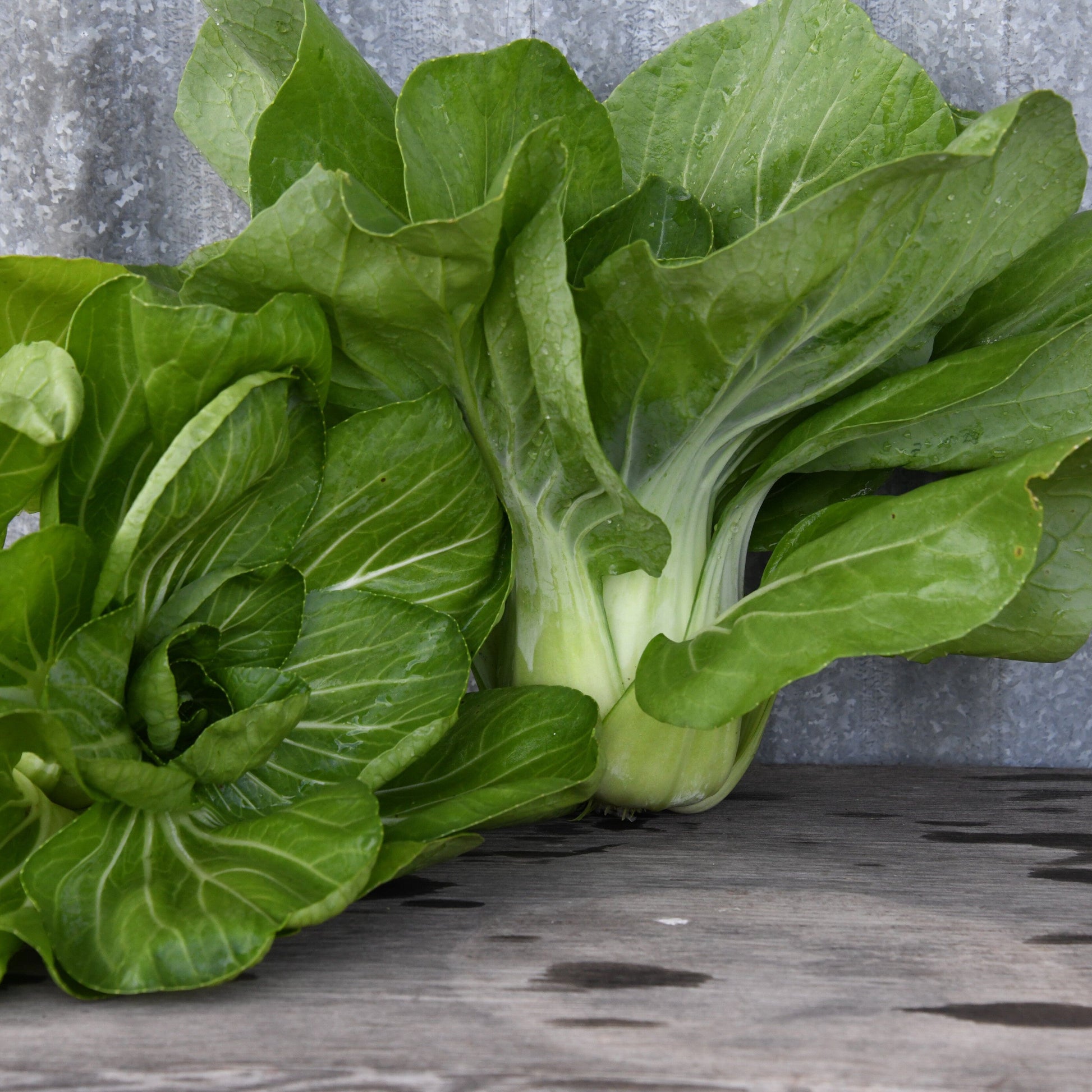 Bunch of green leafy vegetables on a wooden surface with a gray background