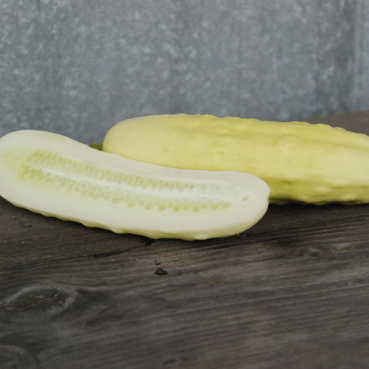 Two silver slicer cucumbers on a wooden surface with a gray background