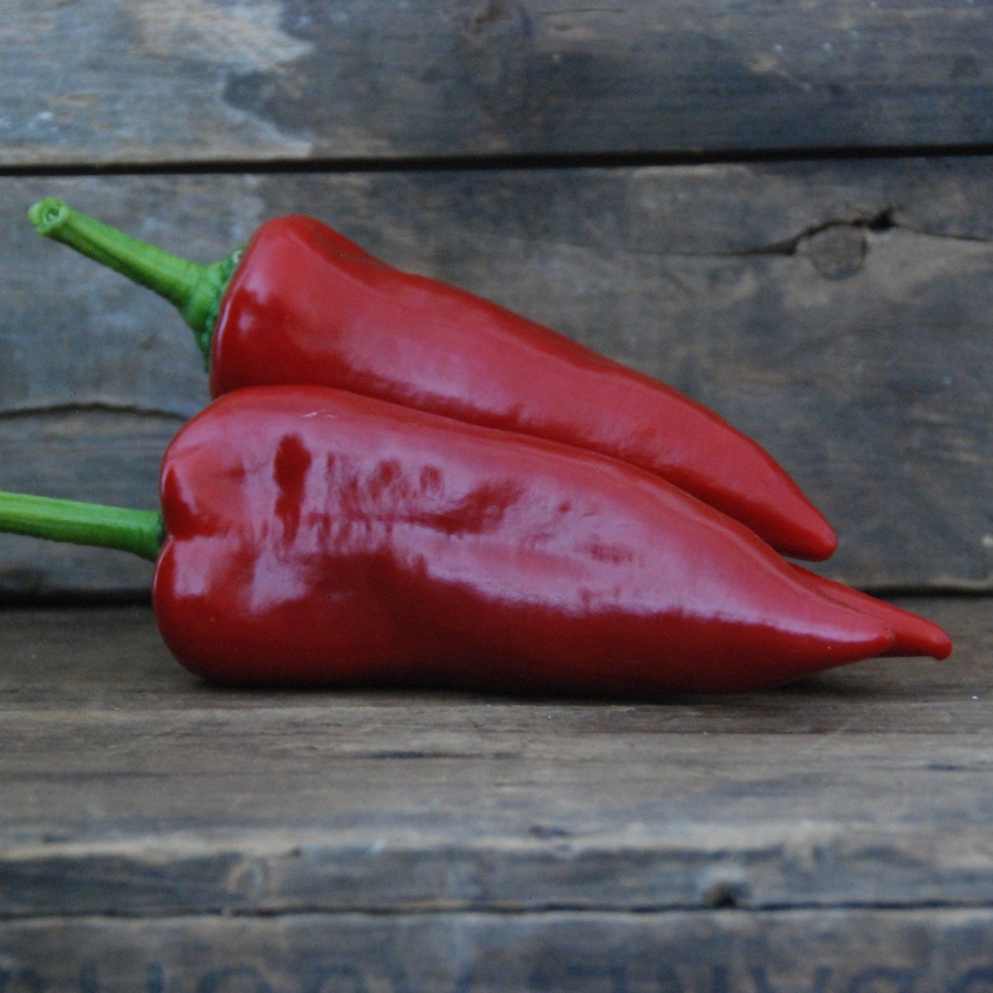 Two red peppers on a wooden surface