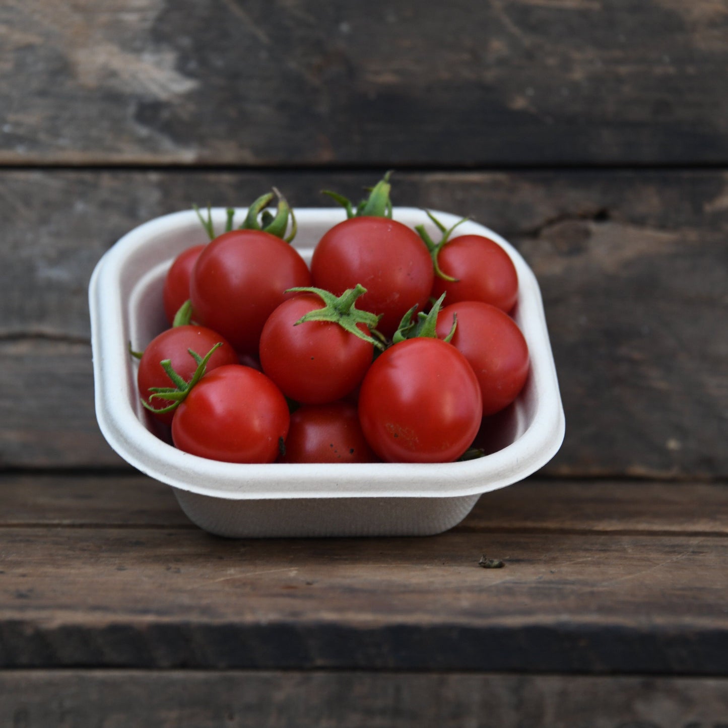 Small container of red tomatoes on a wooden surface