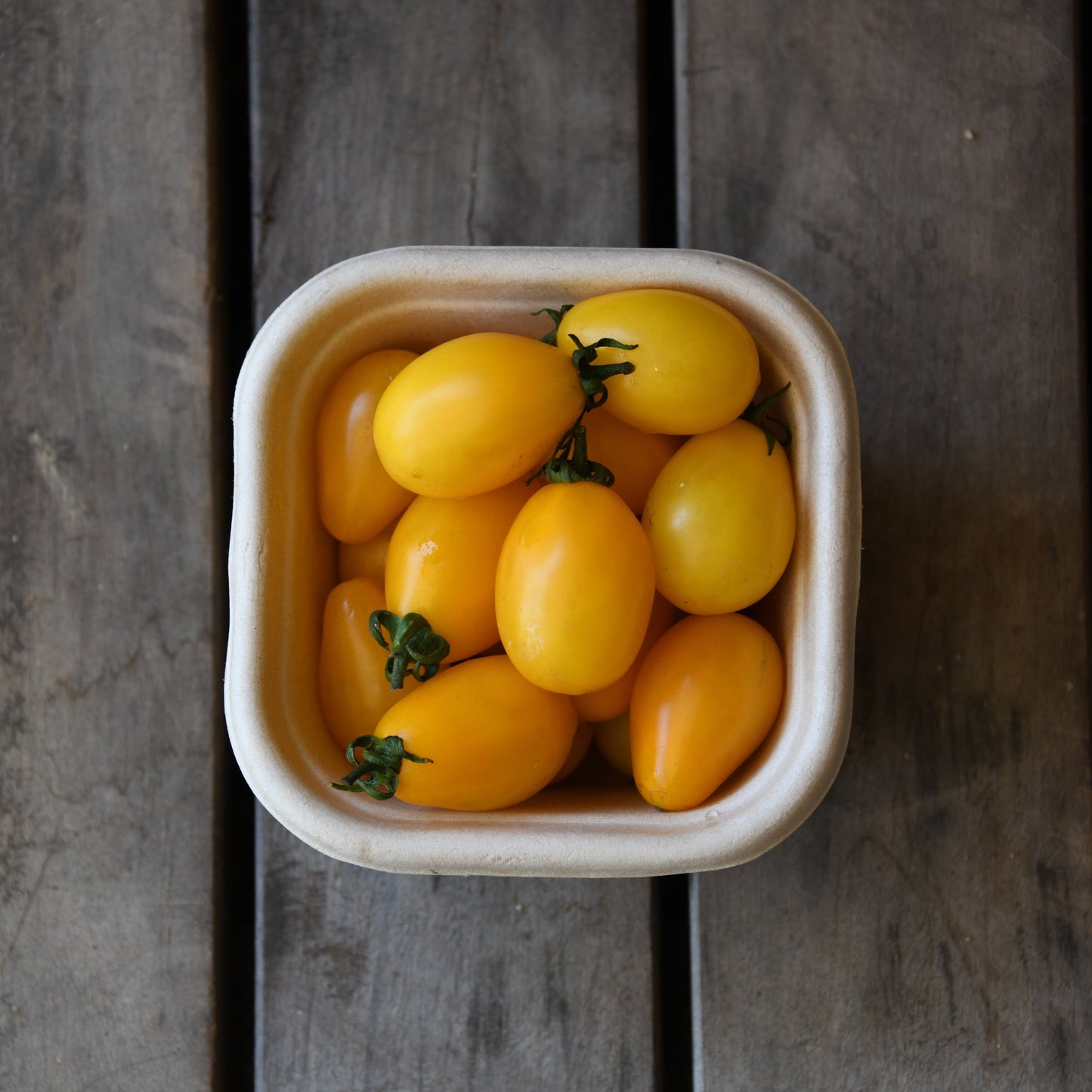 Container of yellow cherry tomatoes on a wooden surface