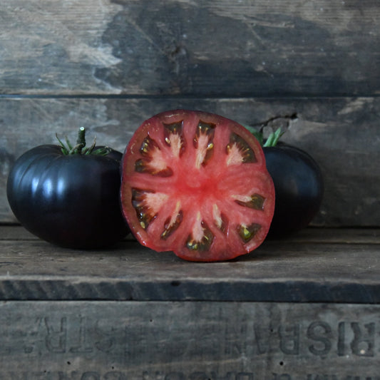 Black tomato and a sliced black tomato on a wooden surface with a rustic background.