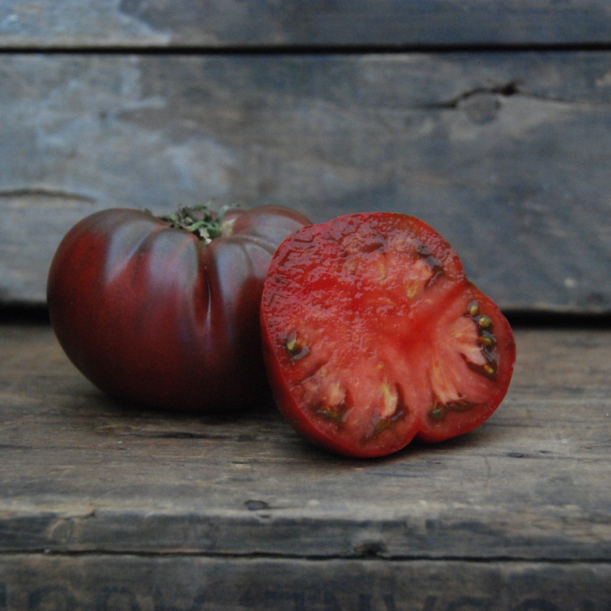Whole and sliced black tomato on a wooden surface with a rustic background