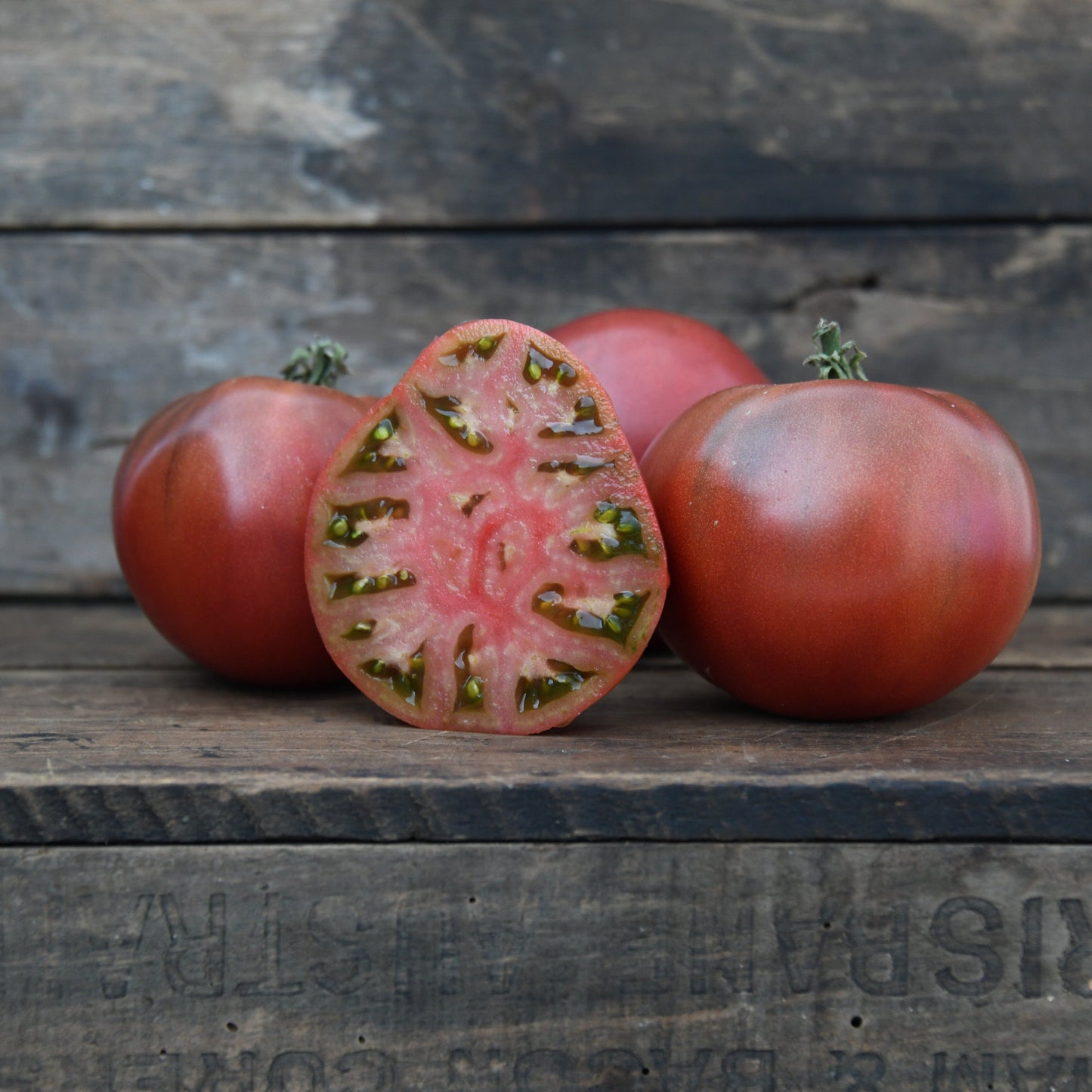 four brown tomatoes on a wooden surface with one sliced open