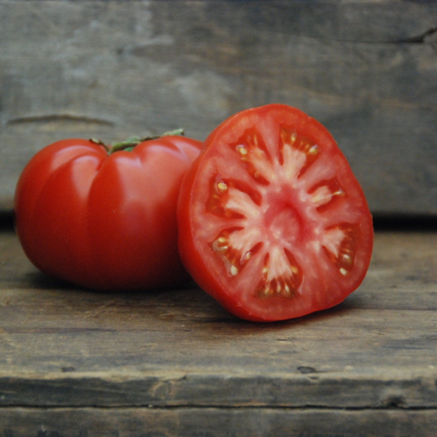 Whole and halved red tomato on a wooden surface with a rustic background