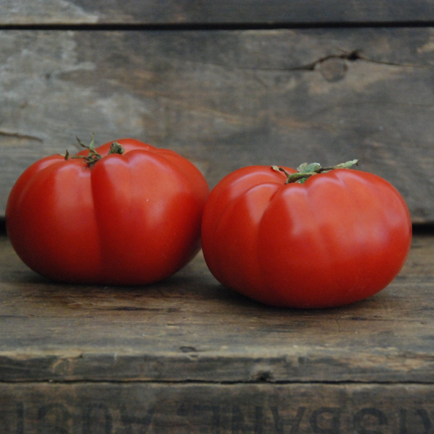 Two red tomatoes on a wooden surface