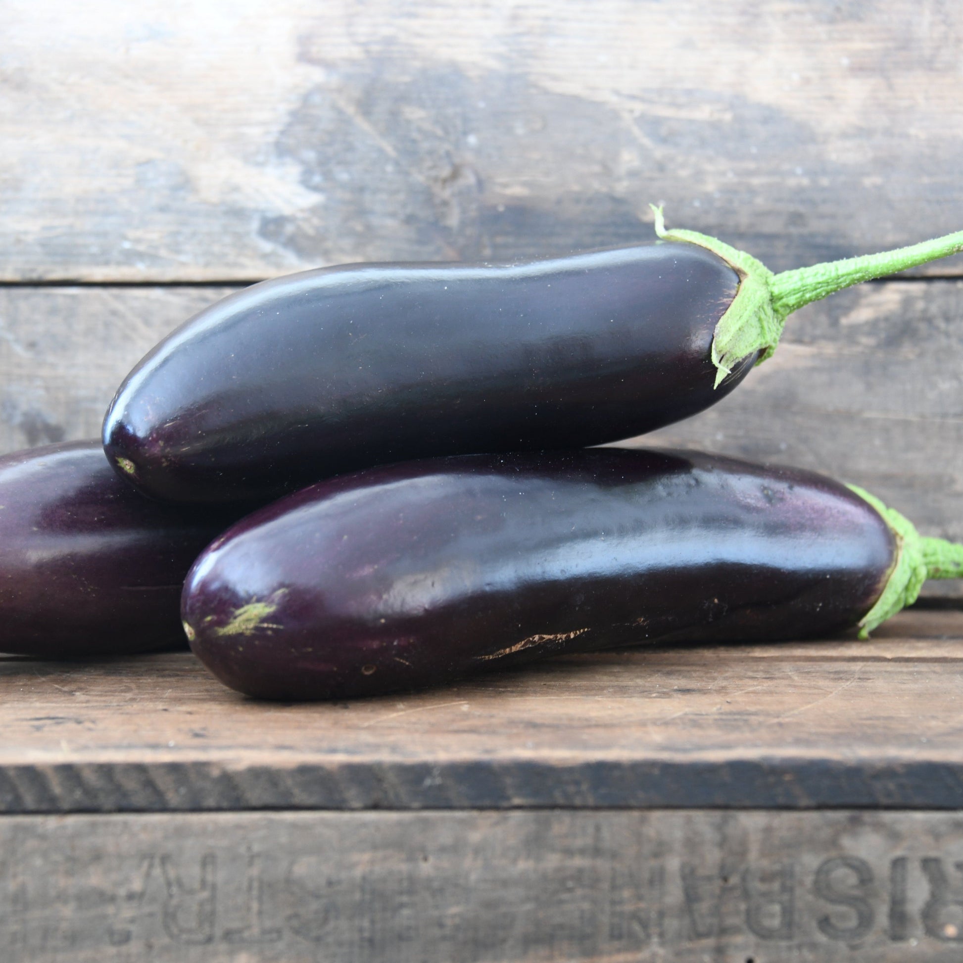 Three eggplants on a wooden surface with a rustic background