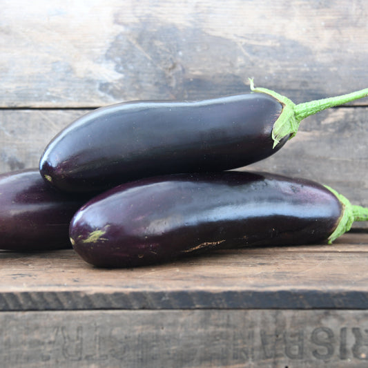 Three eggplants on a wooden surface with a rustic background