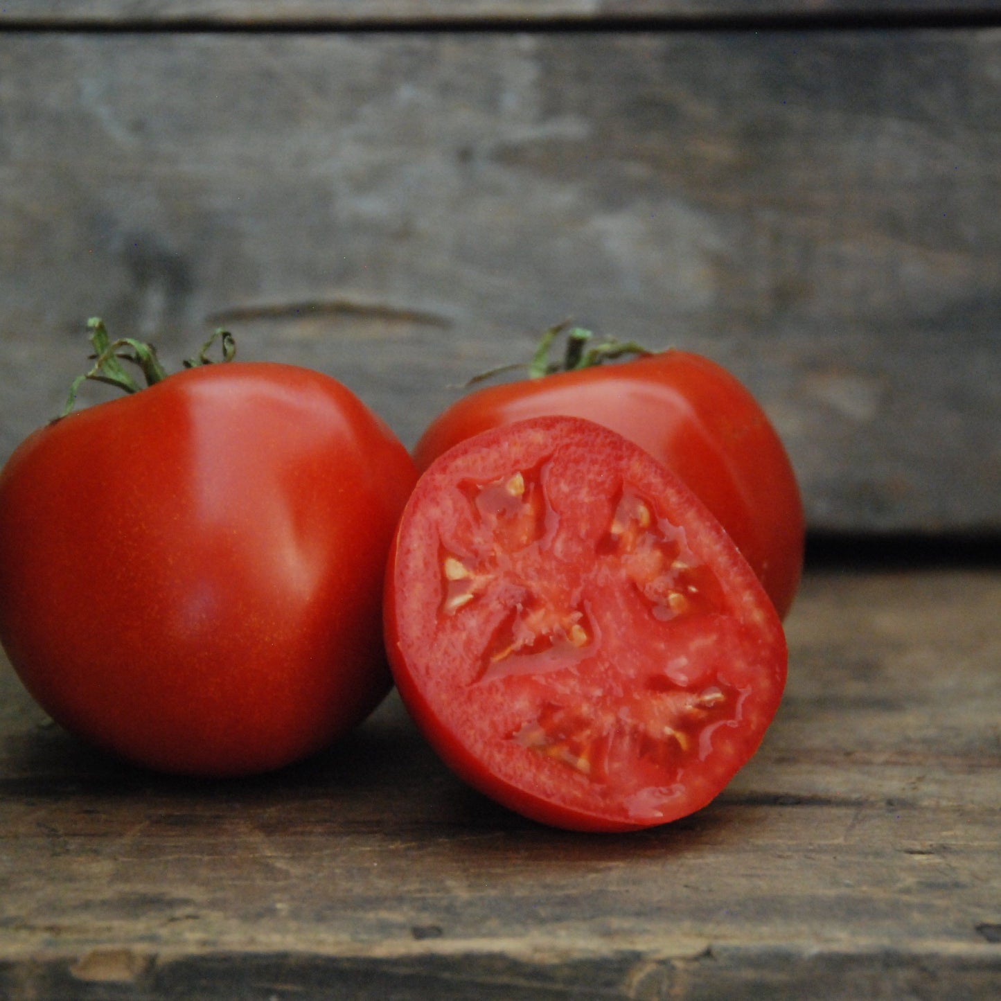 Two tomatoes on a wooden surface, one whole and one cut in half.