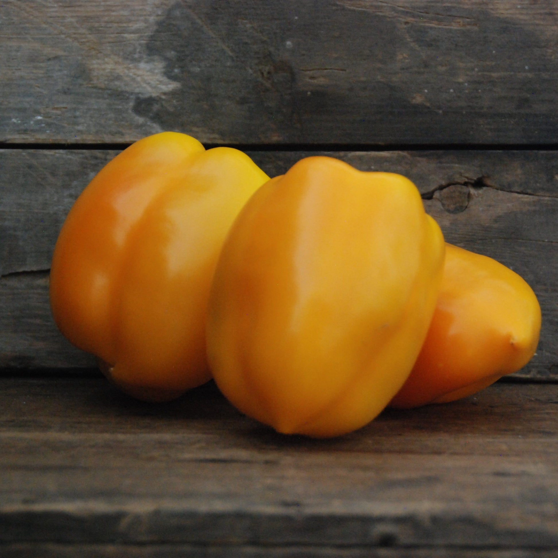 Three yellow peppers on a wooden surface