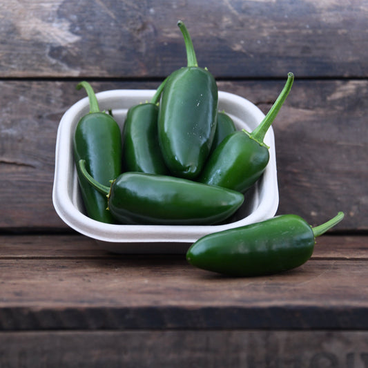Jalapeño peppers in a white container on a wooden surface