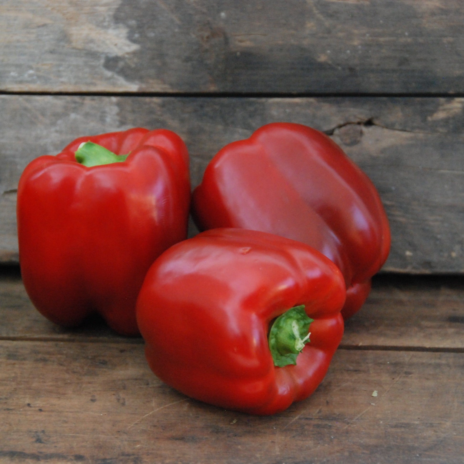 Three red bell peppers on a wooden surface