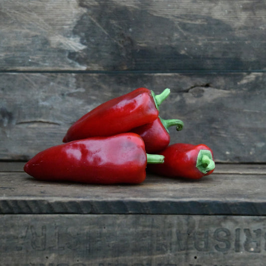 Three red peppers on a wooden surface with a rustic background