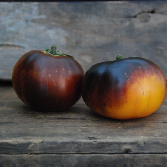 Two dark red and orange tomatoes on a wooden surface