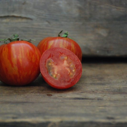 Three tomatoes on a wooden surface with one sliced open, on a rustic background.