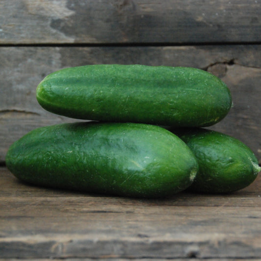 Three green cucumbers stacked on a wooden surface