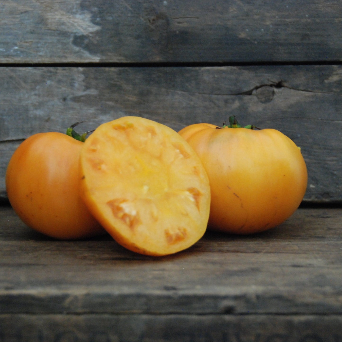 Three yellow tomatoes on a wooden surface with a rustic background