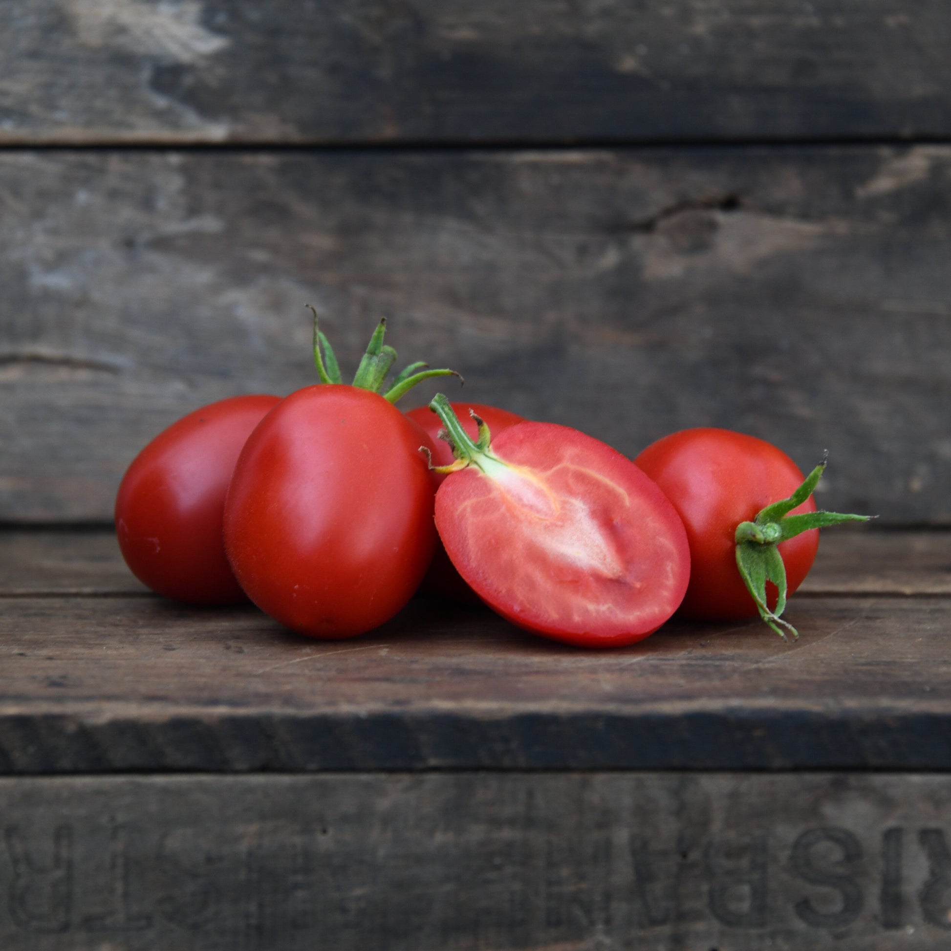 five roma tomatoes on a wooden surface with one cut open