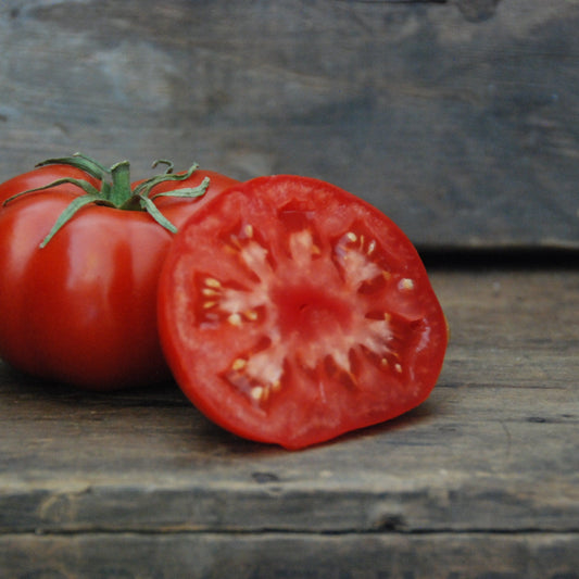 Whole and halved tomato on a wooden surface with a stone background