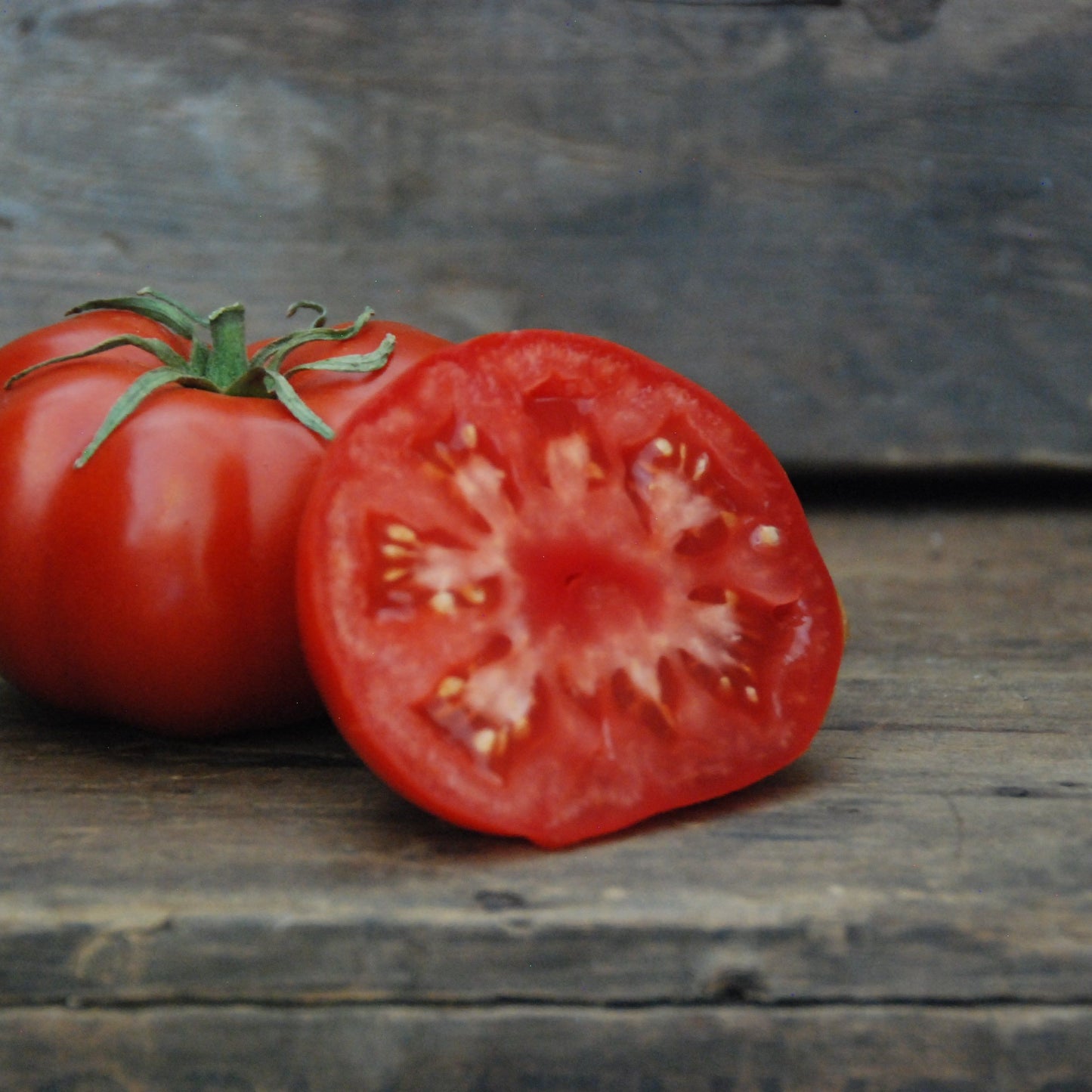 Whole and halved tomato on a wooden surface with a stone background