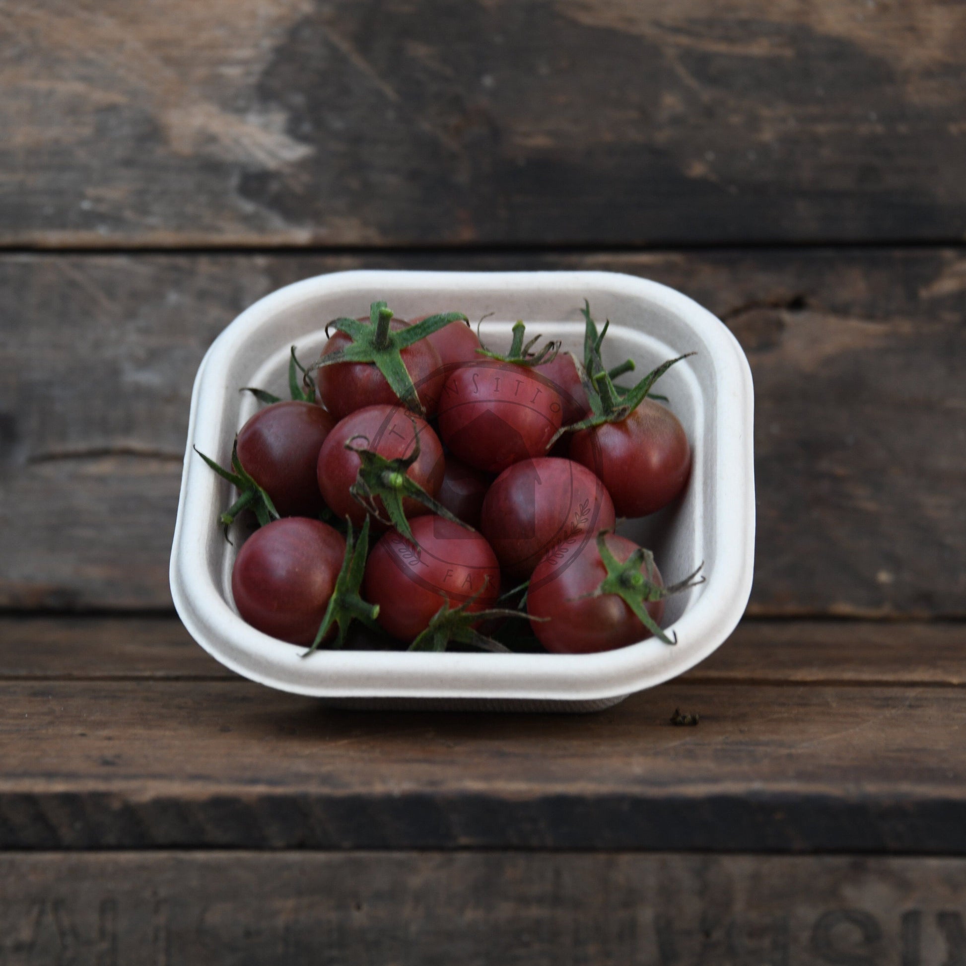 White container with black cherry tomatoes on a wooden surface