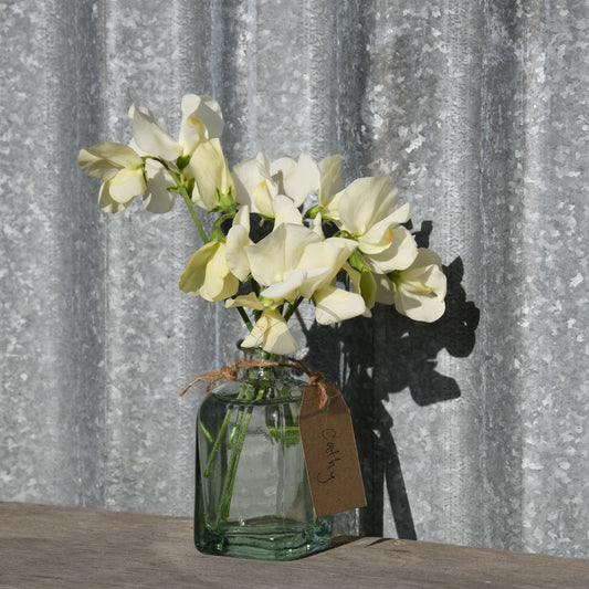 Vase with white flowers and a tag on a wooden surface against a corrugated metal background