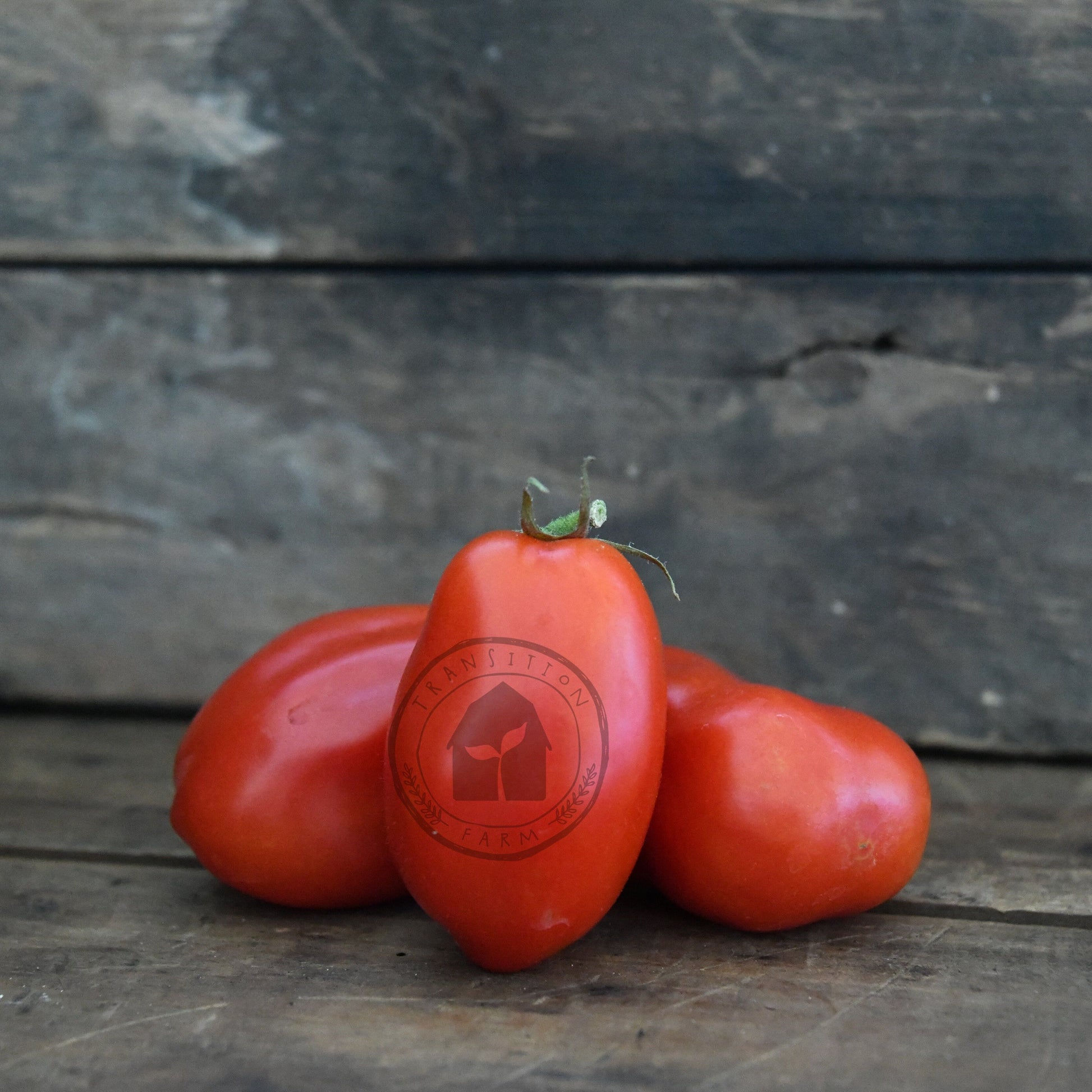 Three red tomatoes with a brand logo on a wooden surface