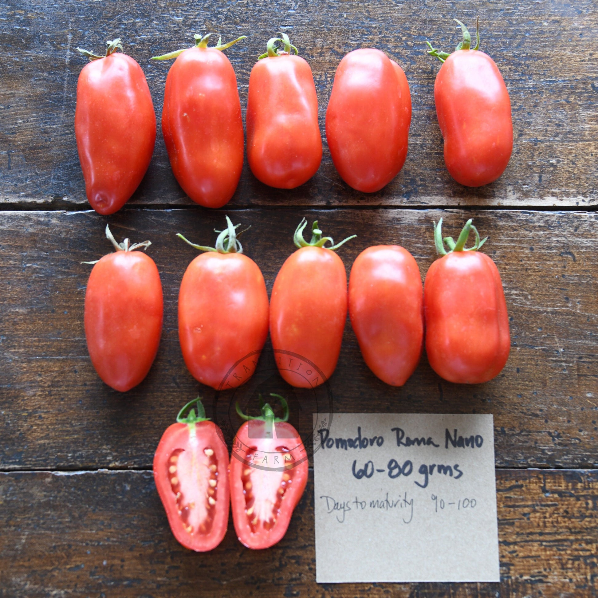Row of red tomatoes on a wooden surface with a label.