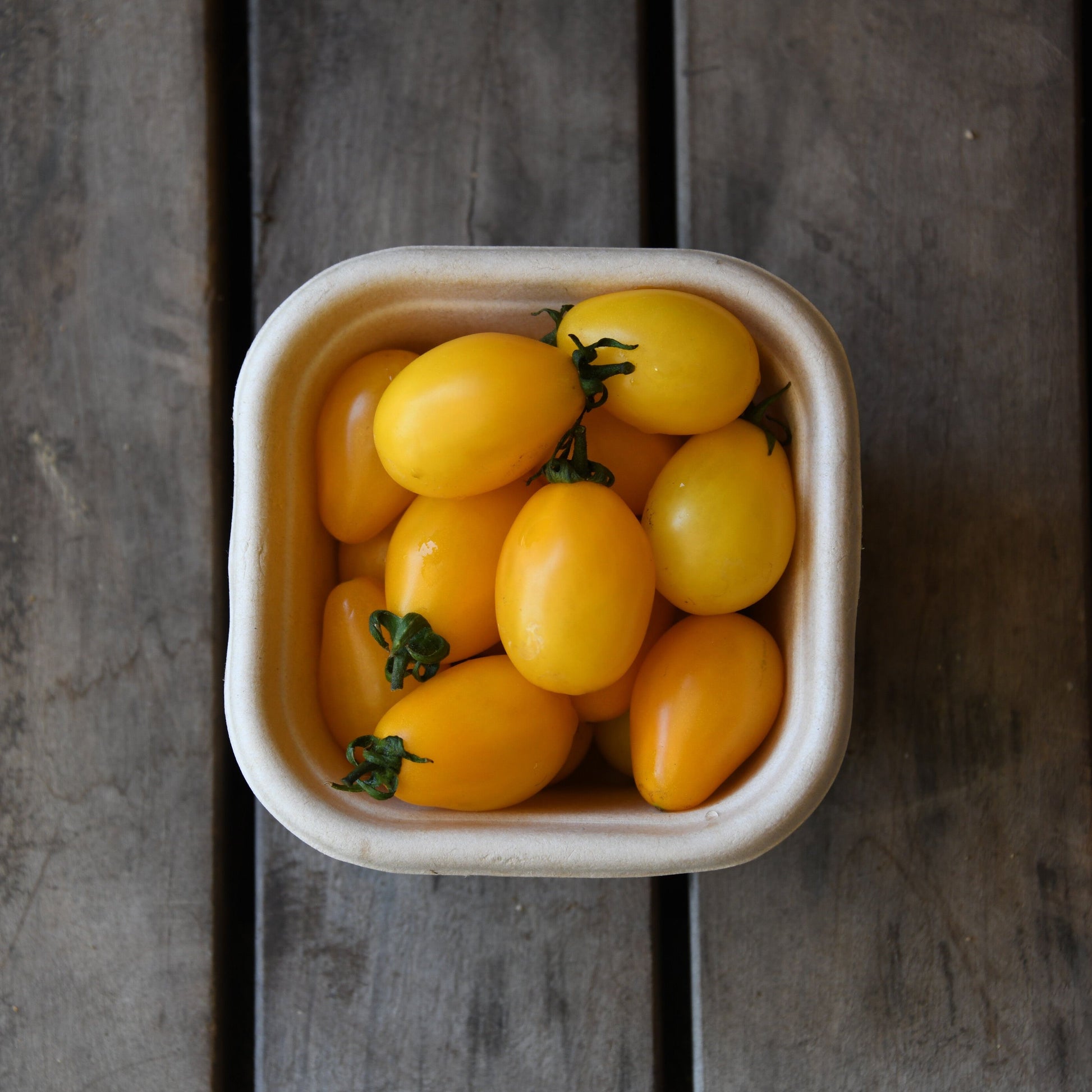 Container of yellow cherry tomatoes on a wooden surface